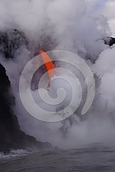 Lava flowing out of cliff into the ocean surounded by white cloud steam