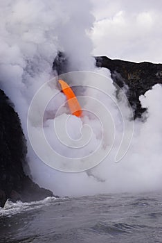 Lava flowing out of cliff into the ocean surounded by white cloud steam