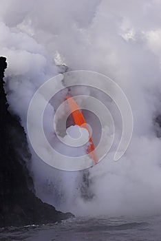 Lava flowing out of cliff into the ocean surounded by white cloud steam