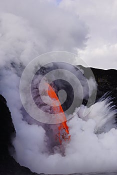 Lava flowing out of cliff into the ocean surounded by white cloud steam