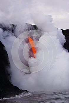 Lava flowing out of cliff into the ocean surounded by white cloud steam