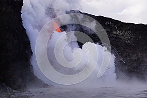 Lava flowing out of cliff into the ocean surounded by white cloud steam