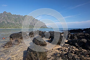 Lava rock beach on Mokolii Island [also known as Chinamans Hat] looking toward Kualoa mountains on the North Shore of Oahu Hawaii