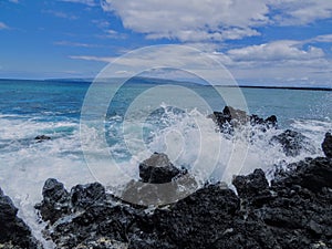 Lava Rock and Coral with Spray of crashing wave in tide pools at Maluaka Beach and Kihei Maui with sky and clouds