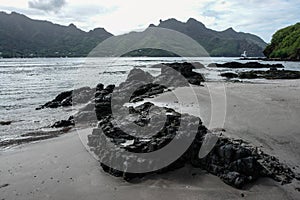 Lava rocks on shoreline with mountains in background, Nuku Hiva, Marquesas Islands, French Polynesia photo