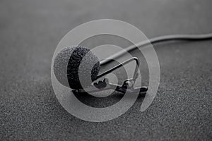 Lavalier or lapel microphone on a black surface, very close-up. The details of the grip clip or bra and the sponge against the photo