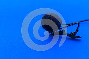 Lavalier or lapel microphone on a blue surface, very close-up. The details of the grip clip or bra and the sponge against the wind photo