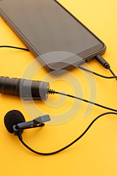 Lavalier or lapel microphone on a colored surface plugged into a cell phone, portrait view . Details of the grip clip or fastener photo