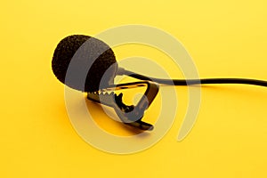 Lavalier or lapel microphone on a yellow surface, very close-up. The details of the grip clip or bra and the sponge against the photo