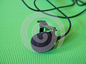 Lavalier Microphone Detail. A black lavalier microphone with foam windscreen and clip on a green background