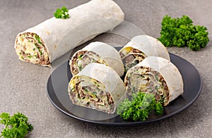 Lavash roll with fish, eggs and parsley on black plate