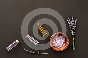 Lavender blossom, glass bottles with extract and essential oil, sea salt on black background, top view, flat lay