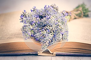 Lavender bouquet laid over an old book on a white wooden background. Vintage style.