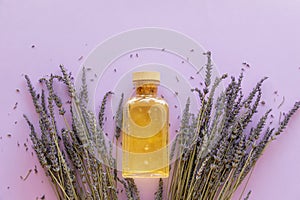 Lavender essential oil, bottle and lavender bouquet on violet background