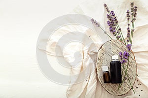 Lavender essential oil bottles on white wooden rustic table with fabric, fresh lavender flowers. Aromatherapy treatment, natural