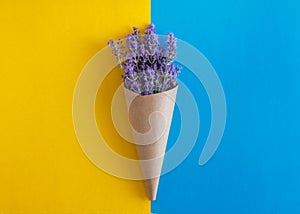 lavender flowers bouquet in parchment paper cone on a yellow and blue isolated background. Copy space. Flat lay. Minimalism. Art