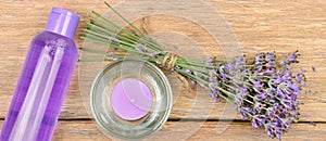 Lavender flowers, scented candle and lavender shampoo on a wooden table. Wide photo