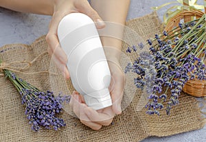 Lavender moisturizer. Empty white tube with lavender moisturizer in female hands