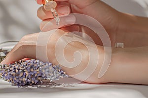Lavender oil dripping from a pipette on hands. Female hands hold a pipette with lavender oil