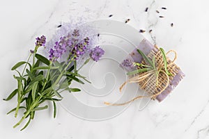 Lavender soap and bunch of fresh flowers on white marble background. Bath body care or spa wellness concept