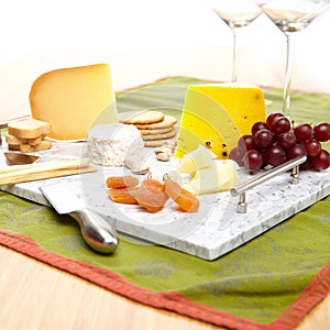 Lavish marble serving tray with cheese, crackers, grapes, apricots, bread sticks,and cheese knives.