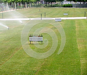 The Grass is Growing sign and lawn sprinkler spaying water over grass. photo