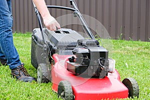 Lawn grass mowing. A man in blue jeans starts a gasoline lawn mower with his hand