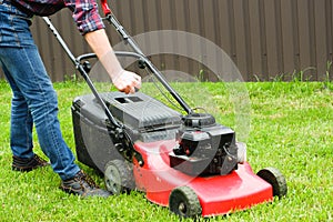 Lawn grass mowing. A man in blue jeans starts a gasoline lawn mower with his hand