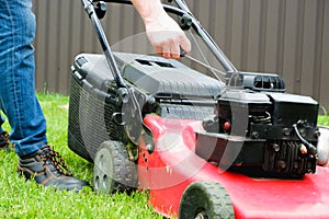 Lawn grass mowing. A man in blue jeans starts a gasoline lawn mower with his hand