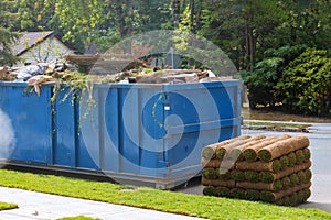 Lawn grass in rolls on pallets against of the street the rolled grass lawn is ready for laying and loaded dumpster near a