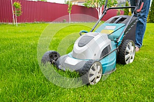 A lawn mover is cutting green grass, the gardener is working with a lawn mower, a close-up, the yard of a private house