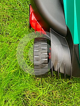 Lawn mower cutting green grass in the backyard. Gardening background.Grass close-up and wheel of a lawn mowing machine, yard care