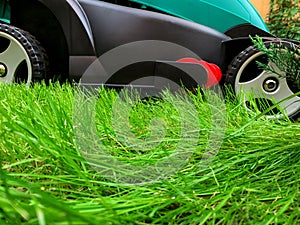 Lawn mower cutting green grass in the backyard. Gardening background.Grass close-up and wheel of a lawn mowing machine, yard care