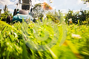 Lawn mower in motion on green grass in garden or backyard. Machine for cutting lawns. Gardening care tools and equipment