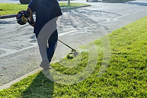 A lawn mower mows fresh, green grass on the lawn near, a municipal worker with lawn mower in his hand.