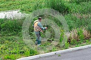 Lawn mower worker cutting grass in green field.Worker mowing tall grass with petrol lawn trimmer in city park or backyard.