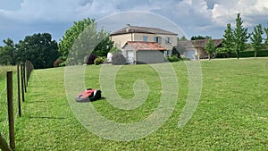 A lawn robot mows the yard. Robotic lawnmower trimming the grass. House yard auto lawn mower cutting grass. Wireless