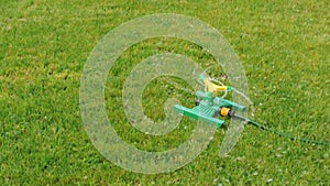 Lawn sprinkler splashing water over green grass