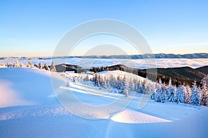 From the lawn with textured snowdrifts there is a view to winter landscape, fair trees in snow, old huts, high mountains, fog.