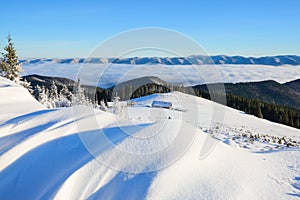 From the lawn with textured snowdrifts there is a view to winter landscape, fair trees in snow, old huts, high mountains, fog.