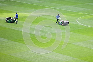 The lawnmower man mows the lawn in a football stadium before the game. Men in baseball caps prepare the field for football games