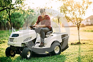 lawnmower tractor with worker doing landscaping works at weekend sunset