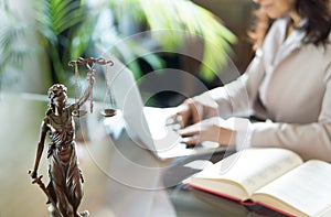 Lawyer office. Statue of Justice with scales and lawyer working on a laptop.