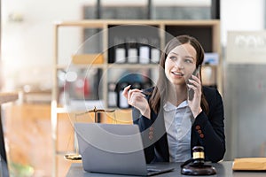 Lawyer woman talking mobile phone and working on tablet and laptop on table in office.