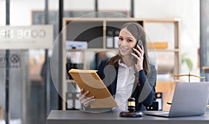 Lawyer woman talking mobile phone and working on tablet and laptop on table in office.