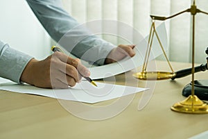 A lawyer working in an office and a judge`s hammer and gold scales in front with a notebook on a legal advisor concept table.