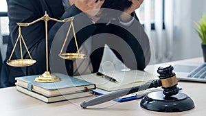 A lawyer working in an office and a judge`s hammer and gold scales in front with a notebook on a legal advisor concept table.