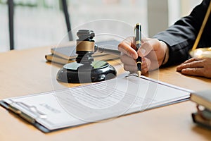 A lawyer working in an office and a judge`s hammer and gold scales in front with a notebook on a legal advisor concept table.