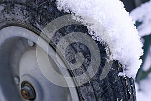 A layer of snow on the wheel of a shopping cart standing on the street