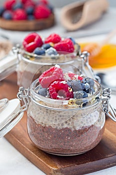 Layered chocolate and peanut butter chia seed pudding in jar, garnished with raspberry, blueberry, honey and coconut flakes,